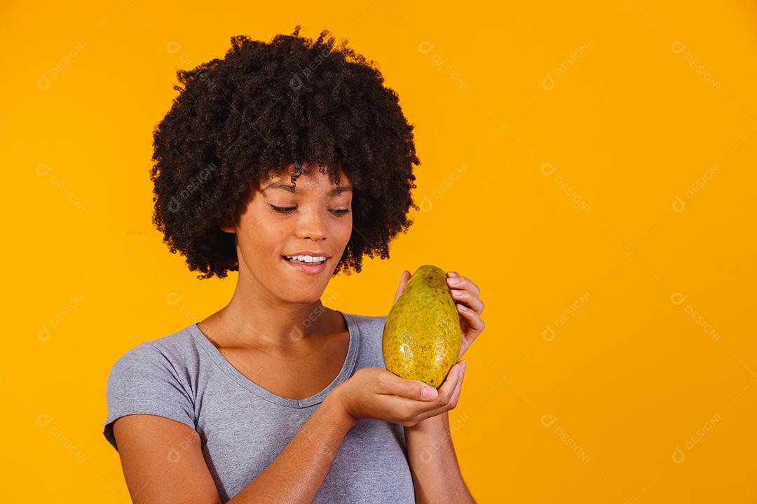Jovem e bela mulher segurando mamão sobre fundo amarelo isolado