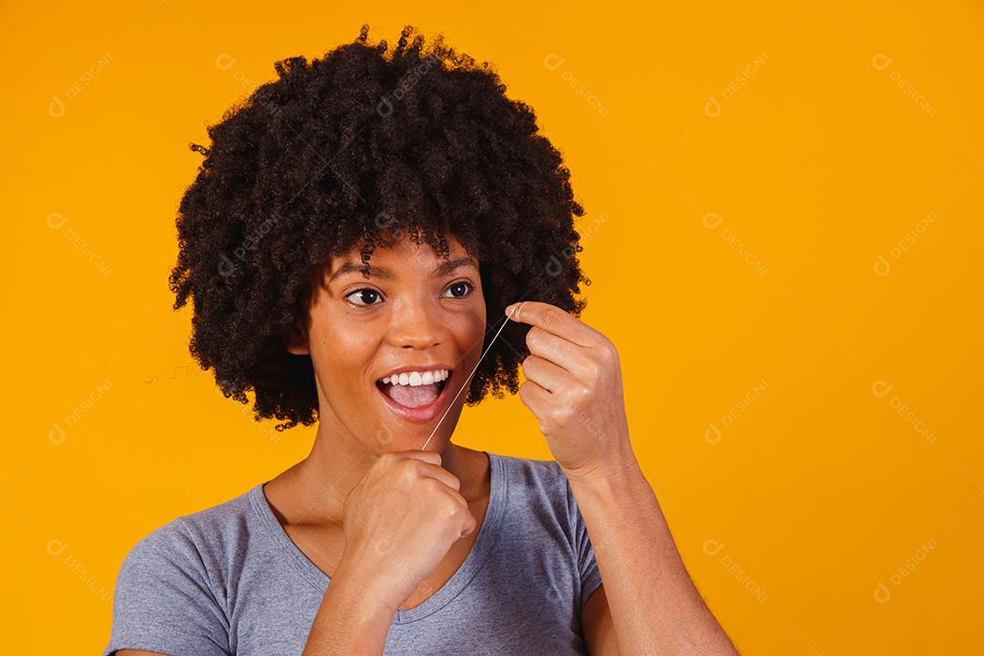 mulher afro passando fio dental nos dentes. conceito de saúde bucal