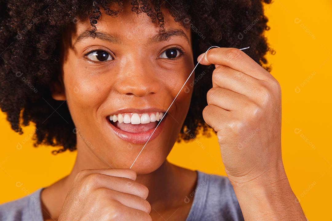 mulher afro passando fio dental nos dentes. conceito de saúde bucal