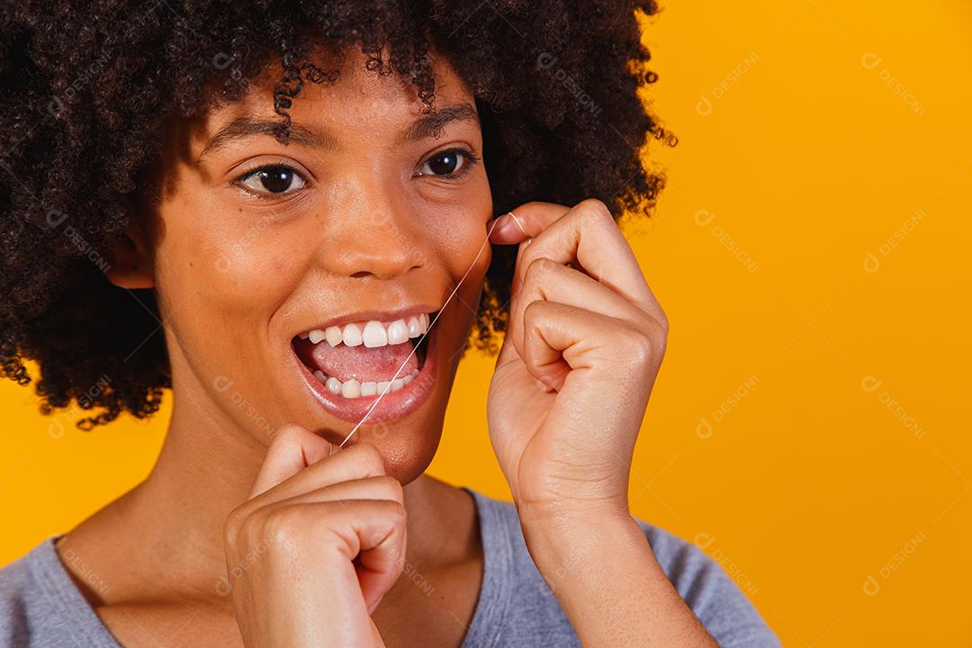 mulher afro passando fio dental nos dentes. conceito de saúde bucal