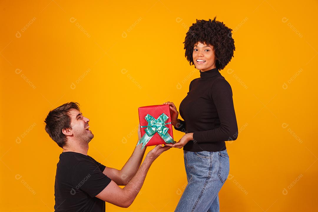 Retrato de um lindo casal em fundo amarelo com um presente