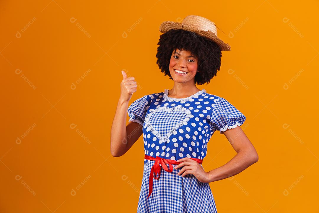 Mulher afro brasileira vestindo roupas típicas para a Festa Junina em fundo amarelo