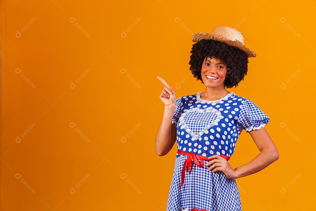 Mulher afro brasileira vestindo roupas típicas para a Festa Junina em fundo amarelo