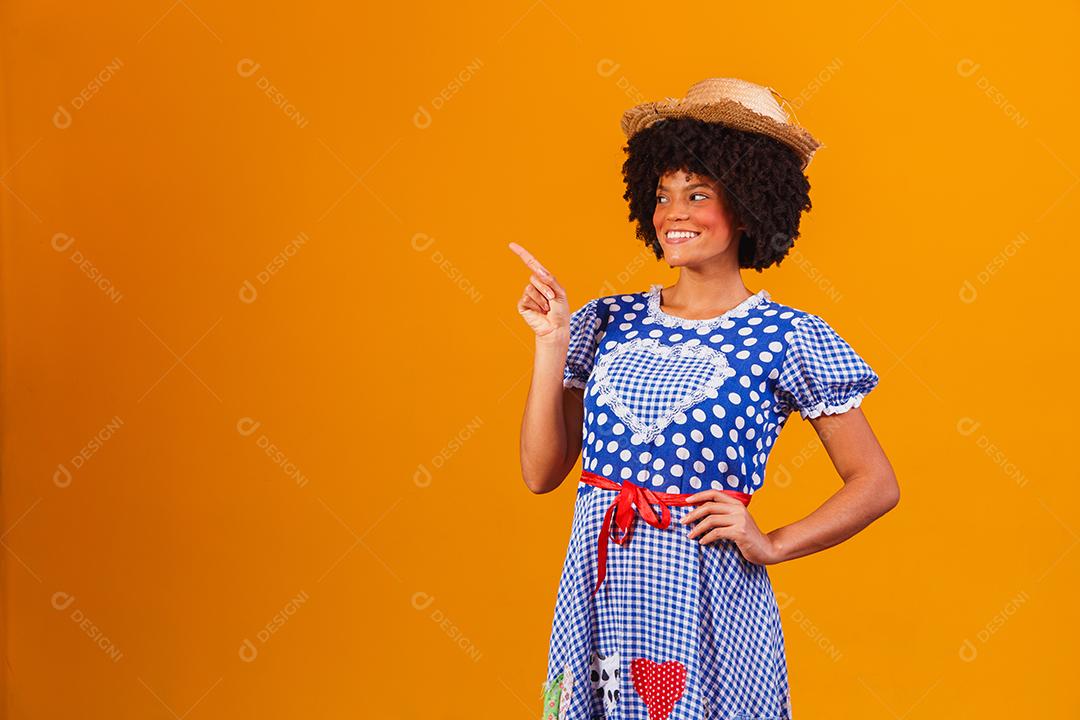 Mulher afro brasileira vestindo roupas típicas para a Festa Junina em fundo amarelo