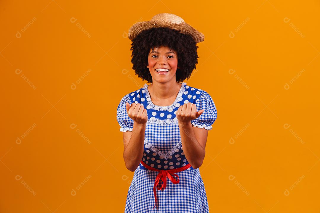 Mulher afro brasileira vestindo roupas típicas para a Festa Junina em fundo amarelo