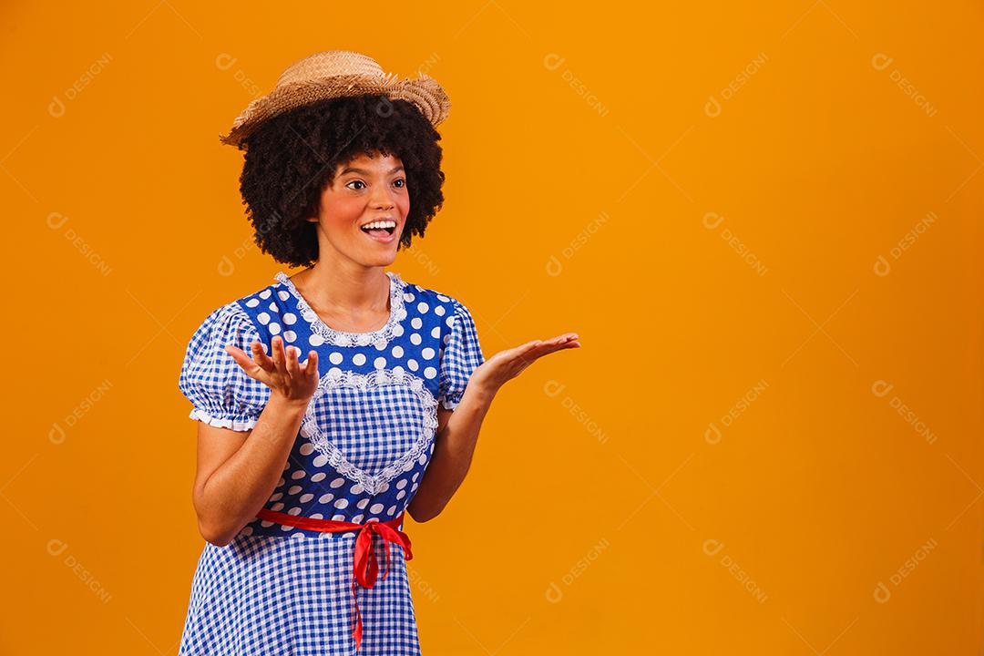 Mulher afro brasileira vestindo roupas típicas para a Festa Junina em fundo amarelo