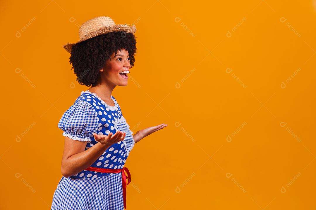 Mulher afro brasileira vestindo roupas típicas para a Festa Junina em fundo amarelo