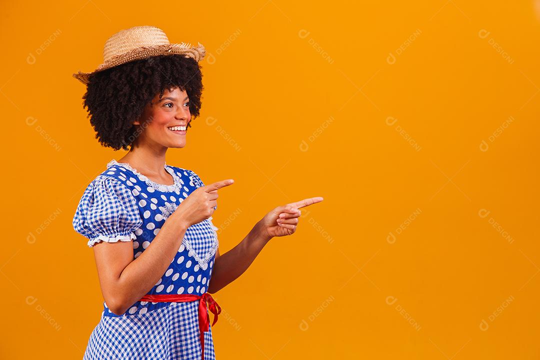 Mulher afro brasileira vestindo roupas típicas para a Festa Junina em fundo amarelo