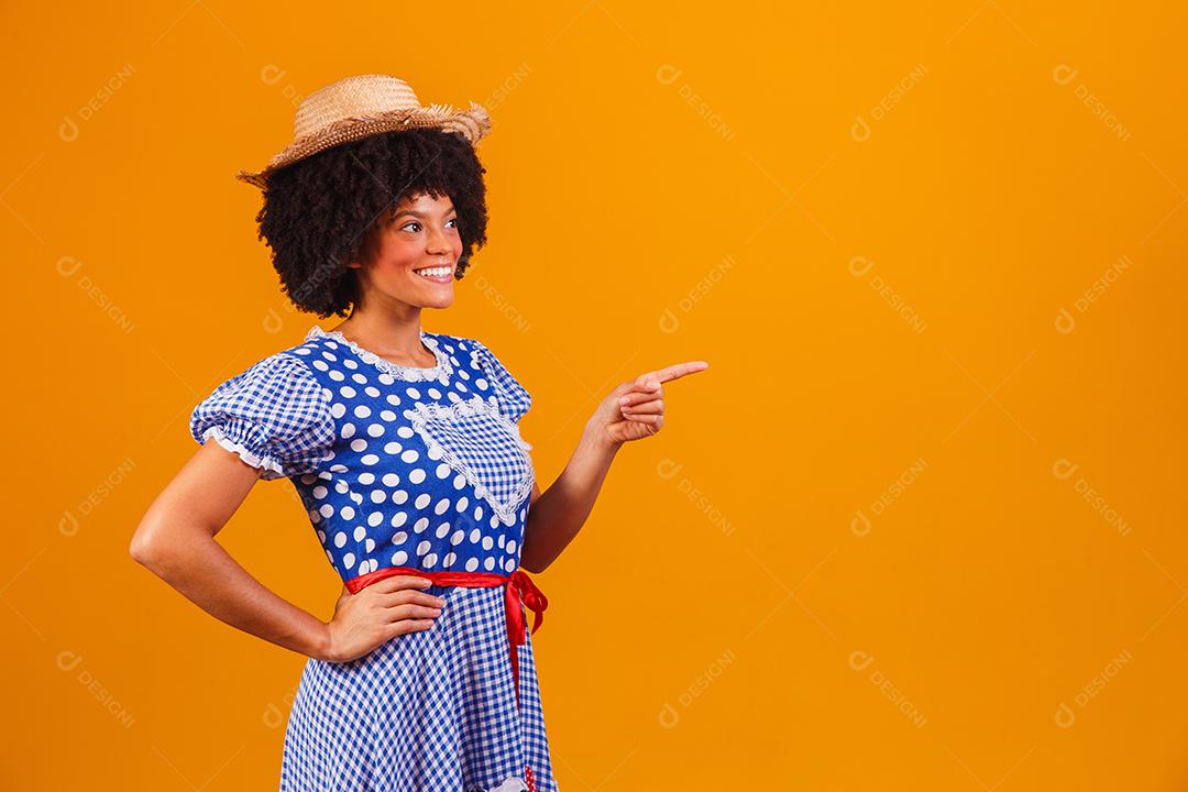 Mulher afro brasileira vestindo roupas típicas para a Festa Junina em fundo amarelo