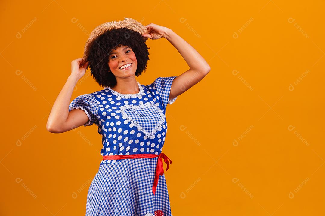 Mulher afro brasileira vestindo roupas típicas para a Festa Junina em fundo amarelo