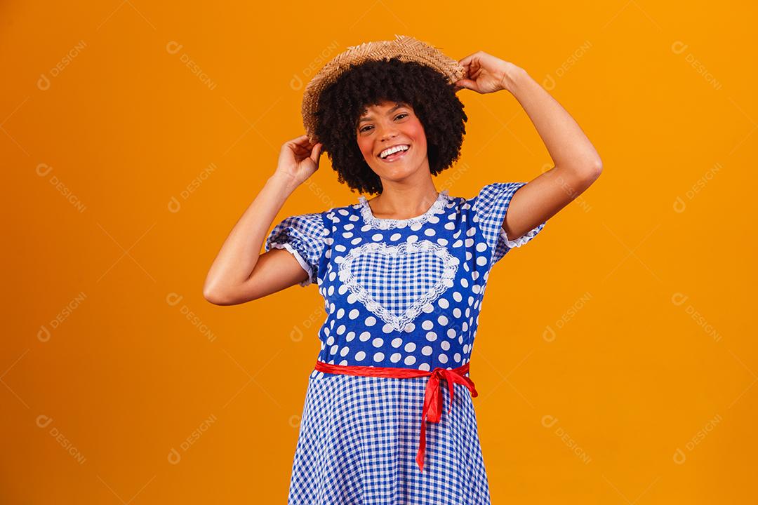 Mulher afro brasileira vestindo roupas típicas para a Festa Junina em fundo amarelo