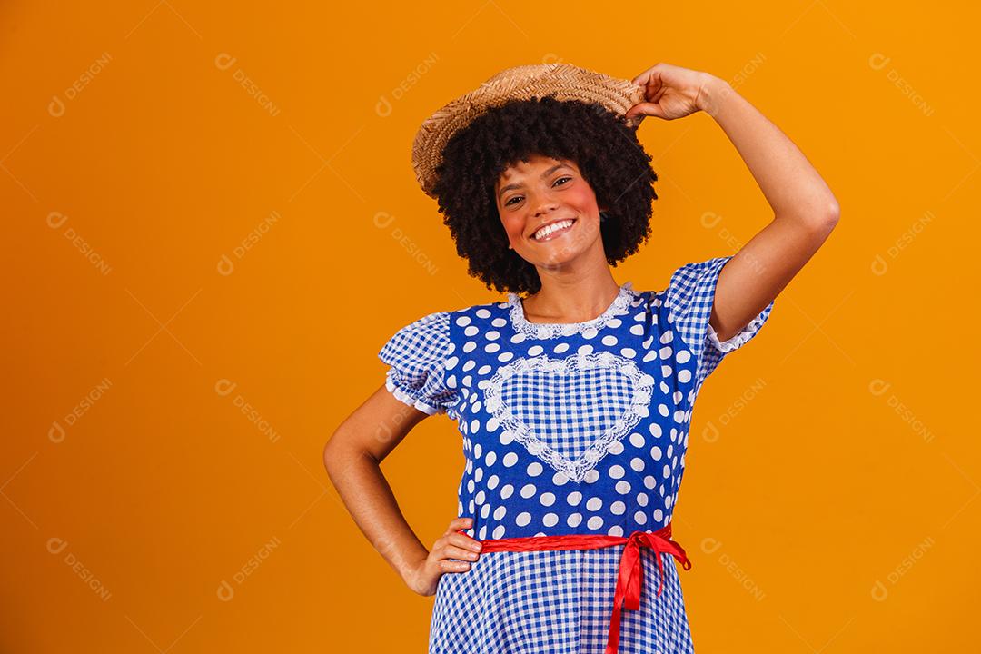 Mulher afro brasileira vestindo roupas típicas para a Festa Junina em fundo amarelo
