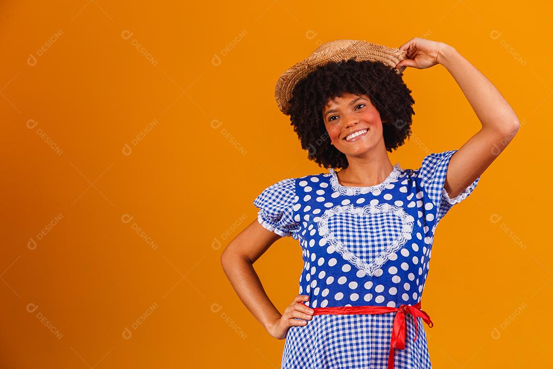 Mulher afro brasileira vestindo roupas típicas para a Festa Junina em fundo amarelo