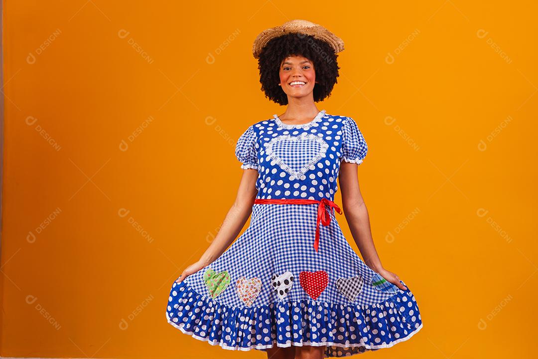 Mulher afro brasileira vestindo roupas típicas para a Festa Junina em fundo amarelo