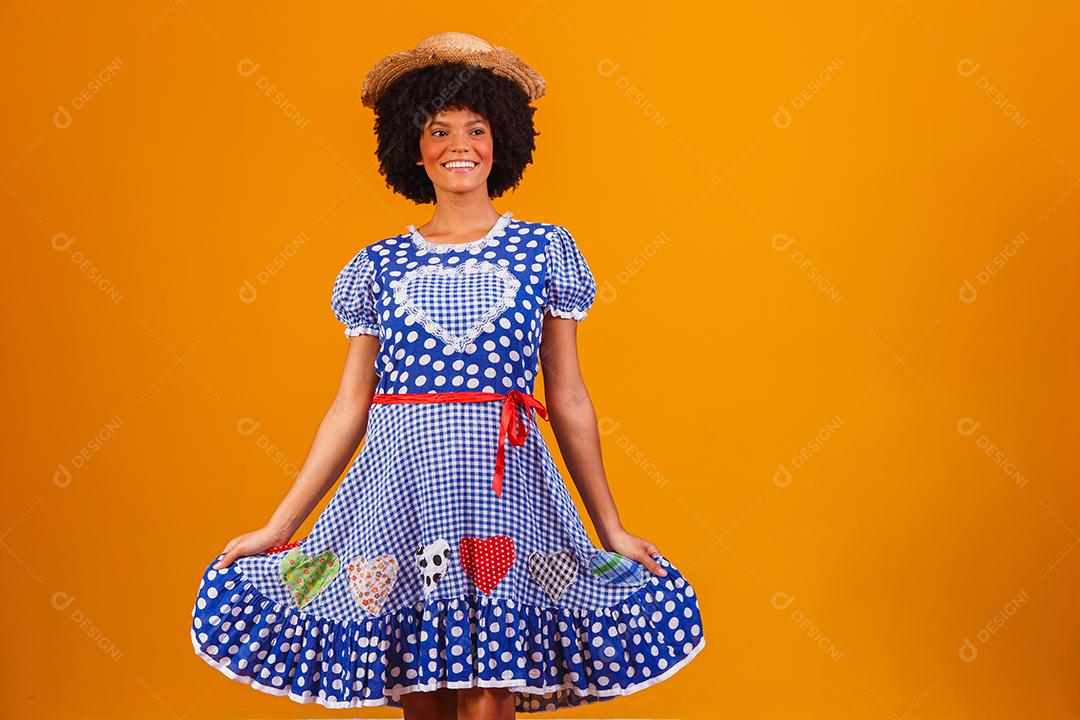 Mulher afro brasileira vestindo roupas típicas para a Festa Junina em fundo amarelo