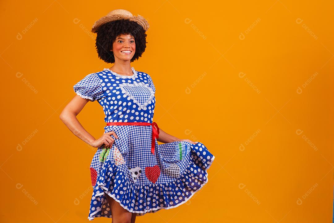 Mulher afro brasileira vestindo roupas típicas para a Festa Junina em fundo amarelo