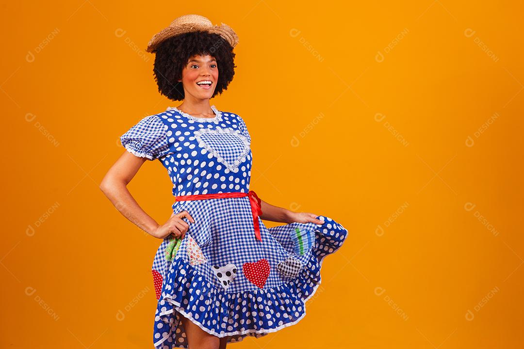 Mulher afro brasileira vestindo roupas típicas para a Festa Junina em fundo amarelo