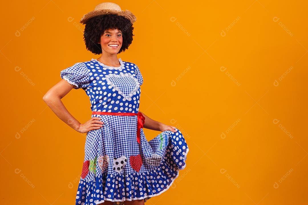 Mulher afro brasileira vestindo roupas típicas para a Festa Junina em fundo amarelo