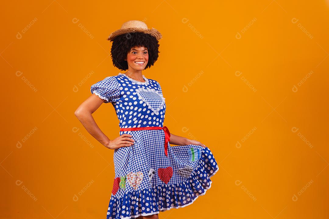 Mulher afro brasileira vestindo roupas típicas para a Festa Junina em fundo amarelo