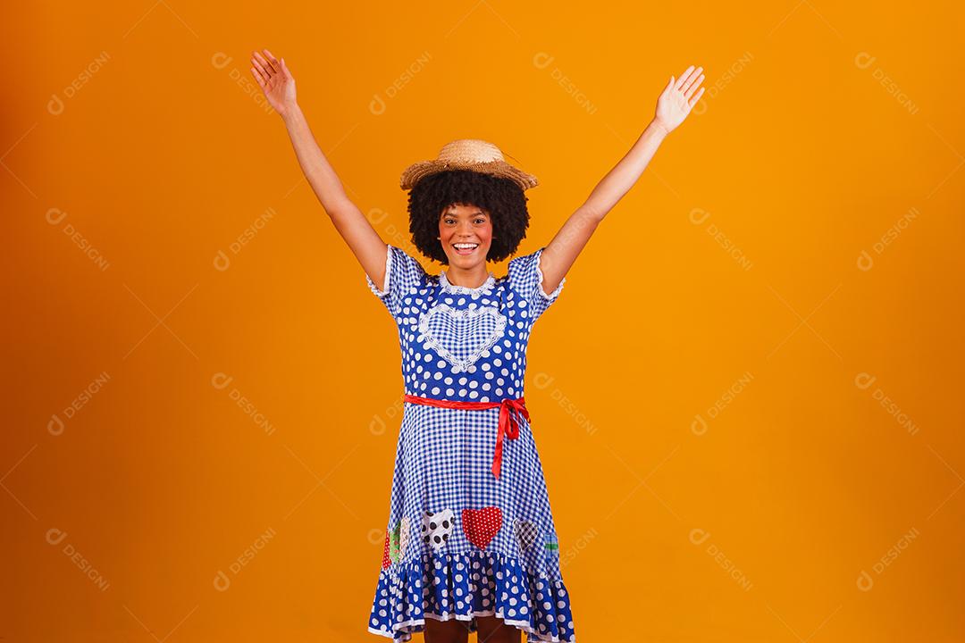 Mulher afro brasileira vestindo roupas típicas para a Festa Junina em fundo amarelo