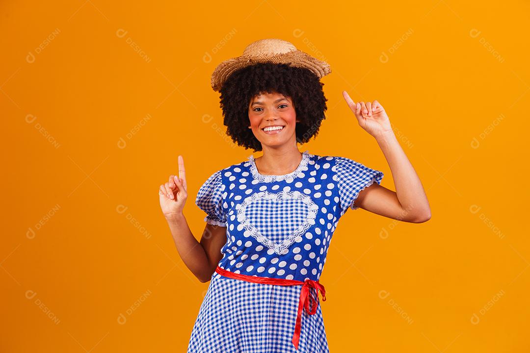 Mulher afro brasileira vestindo roupas típicas para a Festa Junina em fundo amarelo