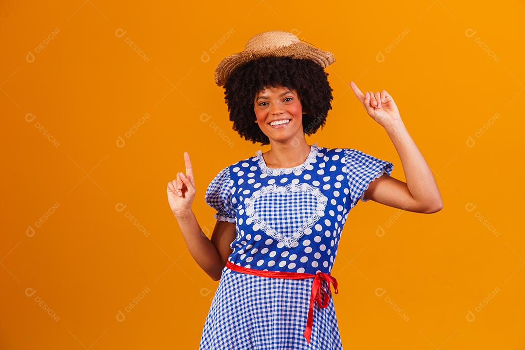 Mulher afro brasileira vestindo roupas típicas para a Festa Junina em fundo amarelo