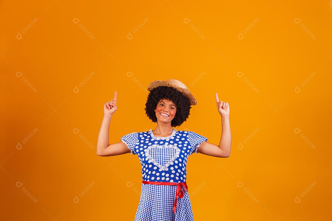 Mulher afro brasileira vestindo roupas típicas para a Festa Junina em fundo amarelo