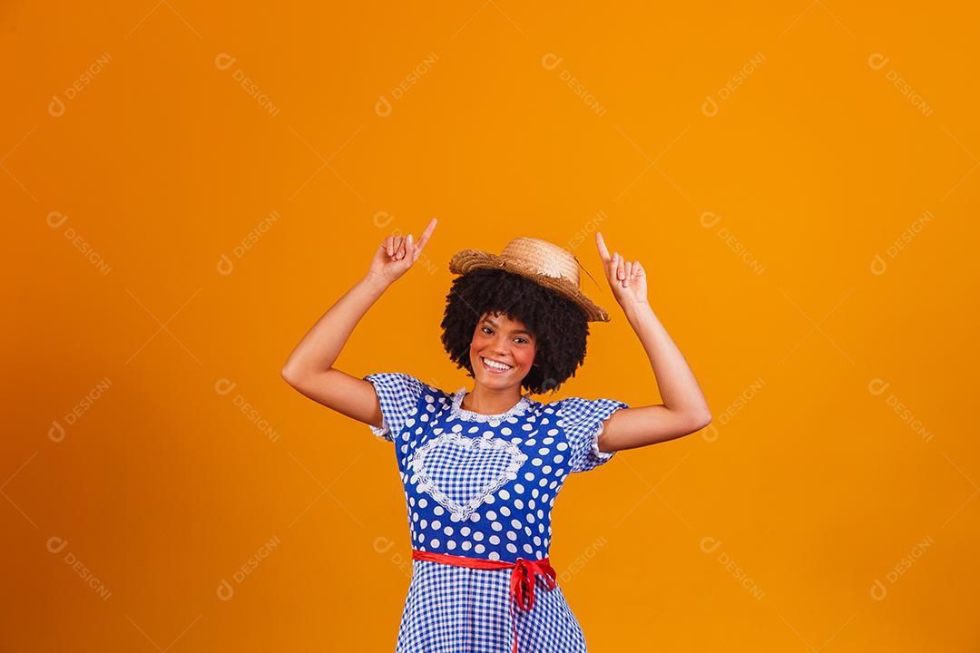 Mulher afro brasileira vestindo roupas típicas para a Festa Junina em fundo amarelo