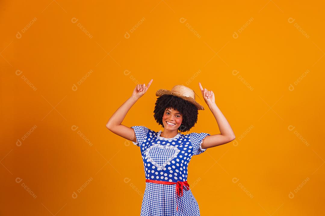 Mulher afro brasileira vestindo roupas típicas para a Festa Junina em fundo amarelo