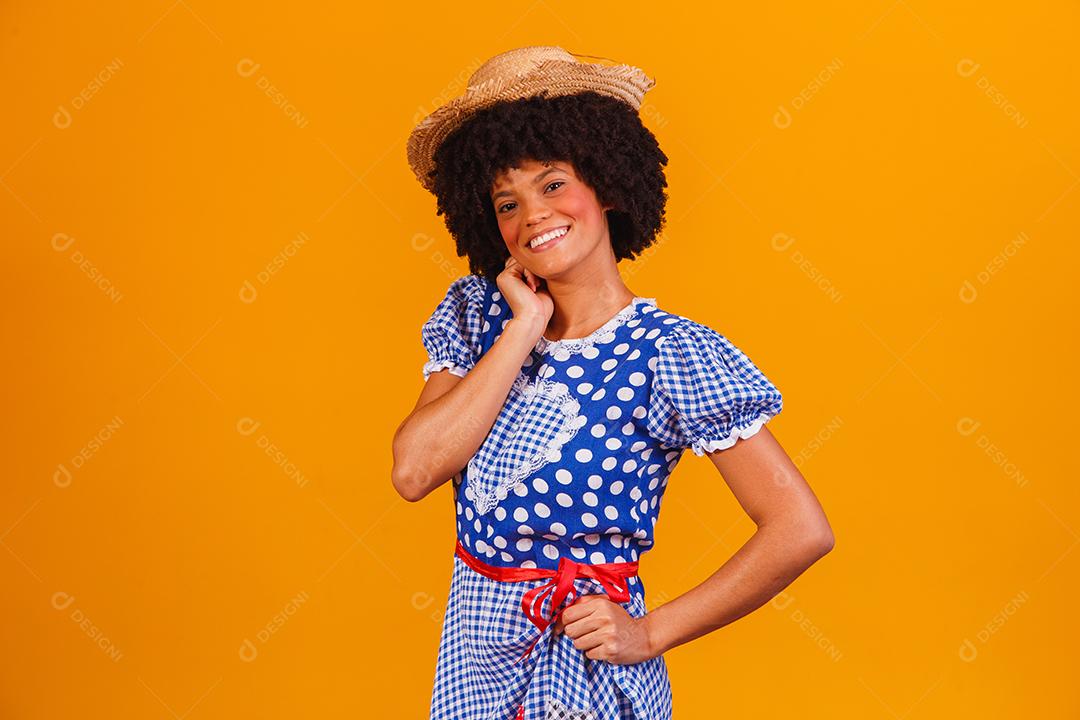 Mulher afro brasileira vestindo roupas típicas para a Festa Junina em fundo amarelo