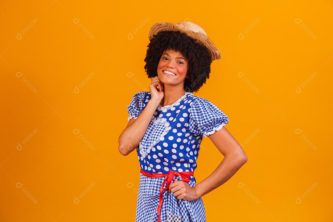 Mulher afro brasileira vestindo roupas típicas para a Festa Junina em fundo amarelo