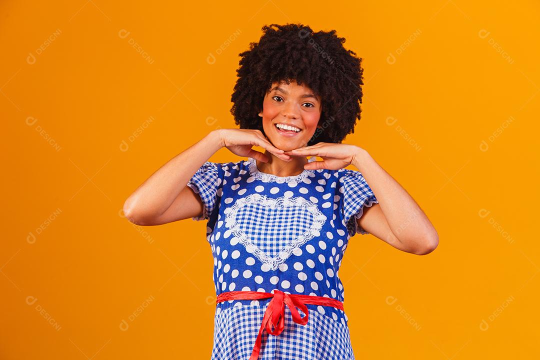 Mulher afro brasileira vestindo roupas típicas para a Festa Junina em fundo amarelo