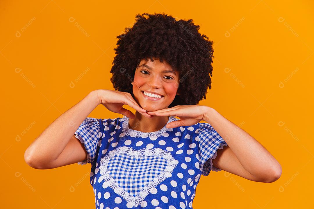 Mulher afro brasileira vestindo roupas típicas para a Festa Junina em fundo amarelo