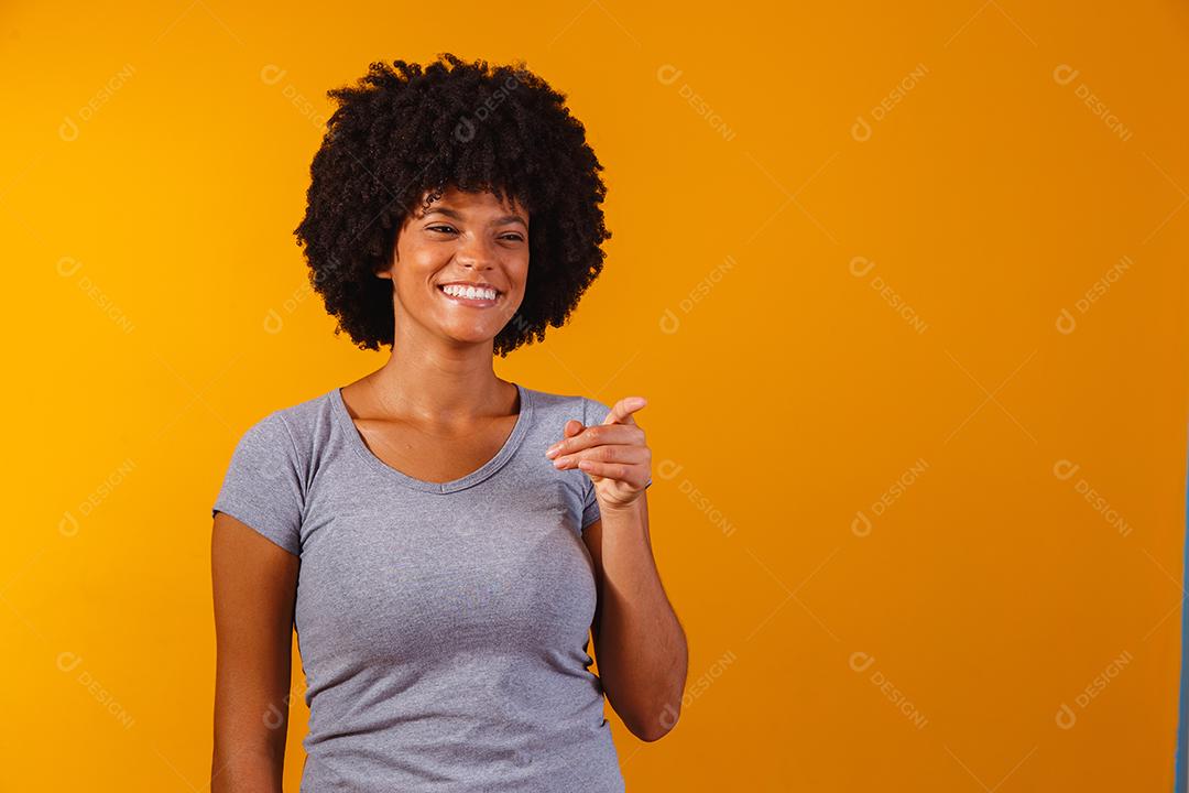 Mulher afro apontando em fundo amarelo