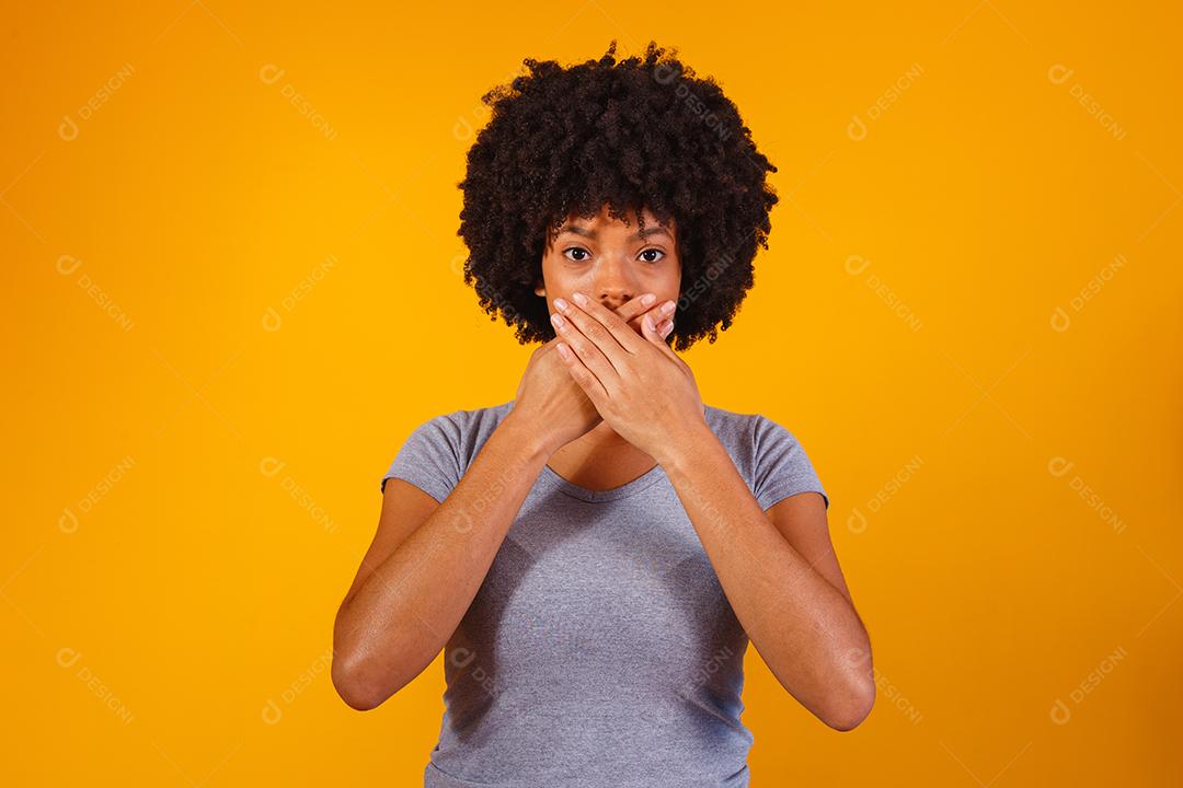 mulher negra em fundo amarelo com a mão na boca, conceito de abuso, feminicídio, racismo e preconceito