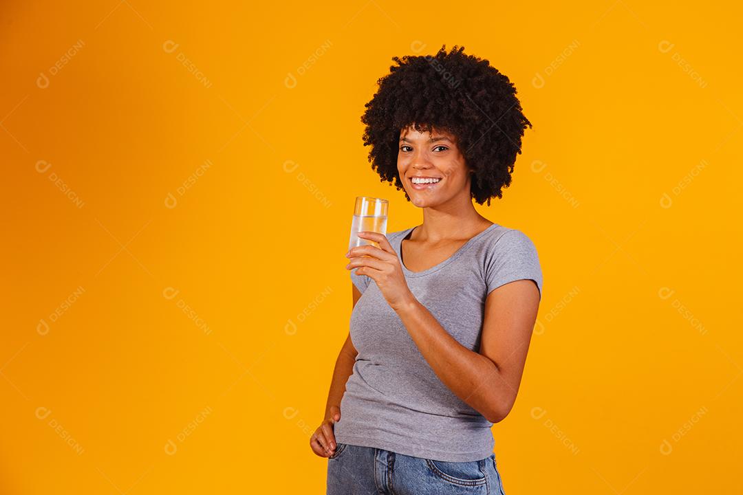 jovem negra bebendo água em fundo amarelo. Moça com copo de água