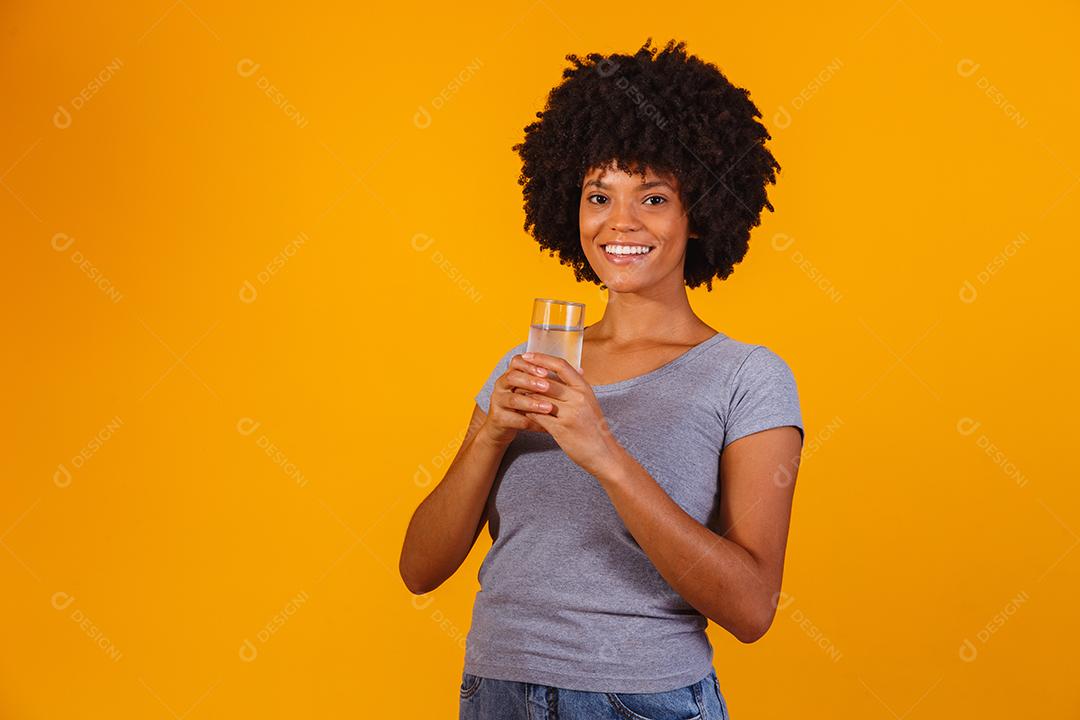 jovem negra bebendo água em fundo amarelo. Moça com copo de água
