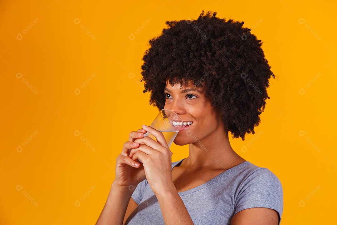 jovem negra bebendo água em fundo amarelo. Moça com copo de água