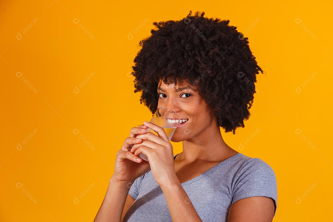 jovem negra bebendo água em fundo amarelo. Moça com copo de água