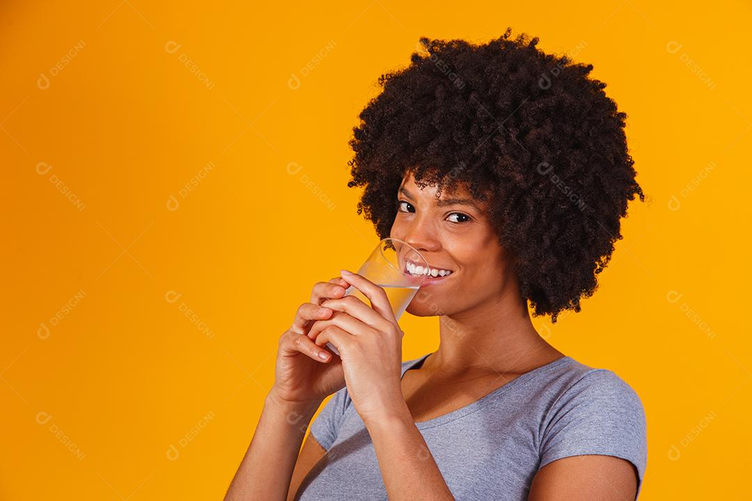 jovem negra bebendo água em fundo amarelo. Moça com copo de água