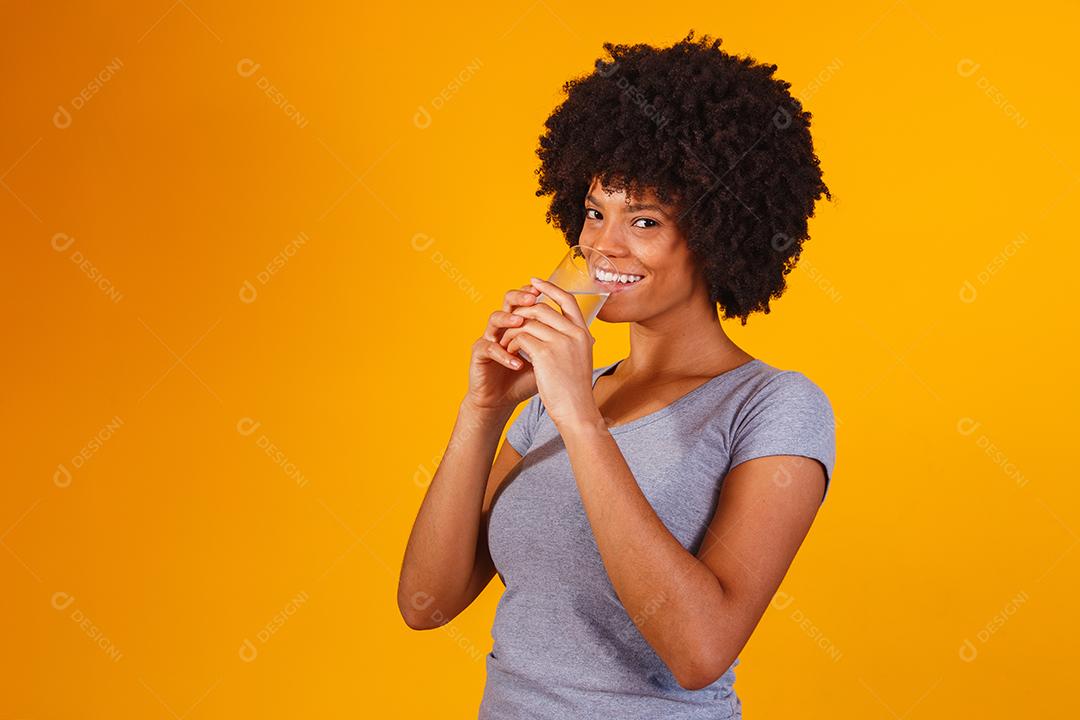 jovem negra bebendo água em fundo amarelo. Moça com copo de água