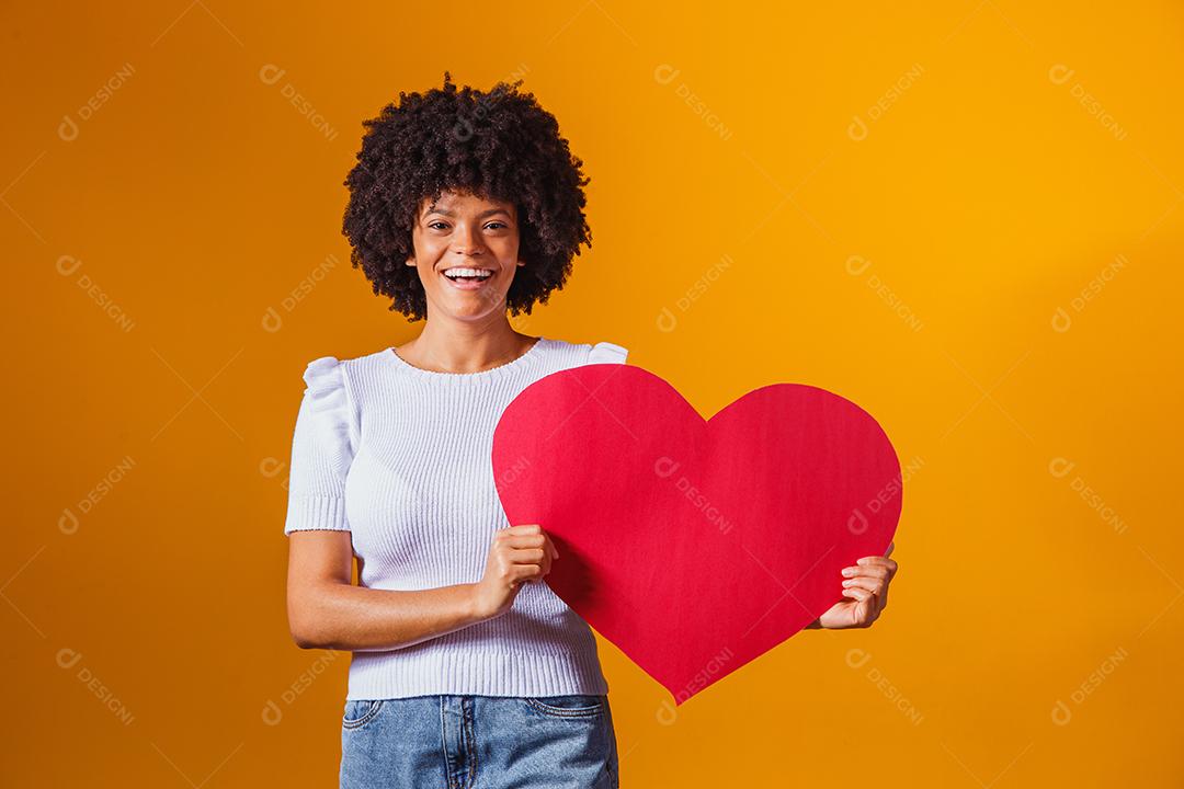 Mulher Afro sorridente segurando um grande cartão de coração vermelho