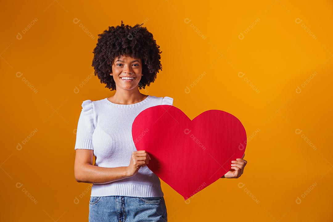 Mulher Afro sorridente segurando um grande cartão de coração vermelho