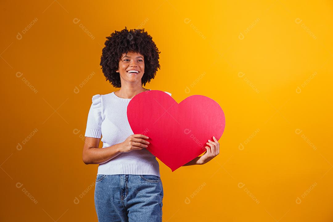 Mulher Afro sorridente segurando um grande cartão de coração vermelho