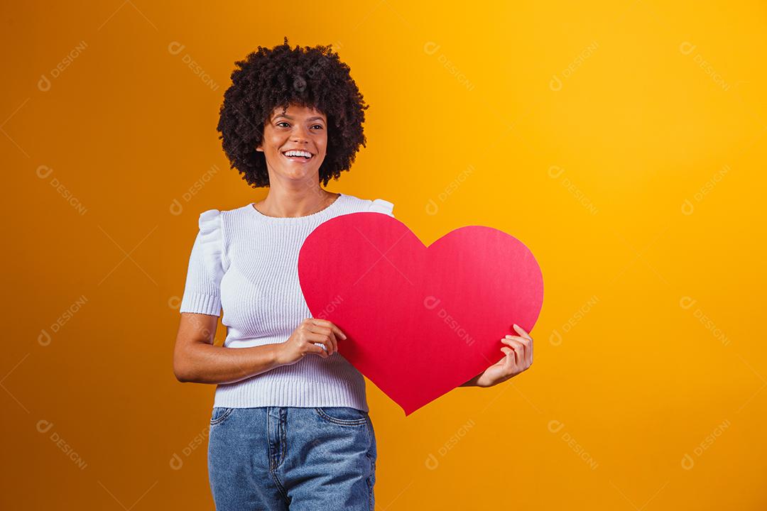 Mulher Afro sorridente segurando um grande cartão de coração vermelho