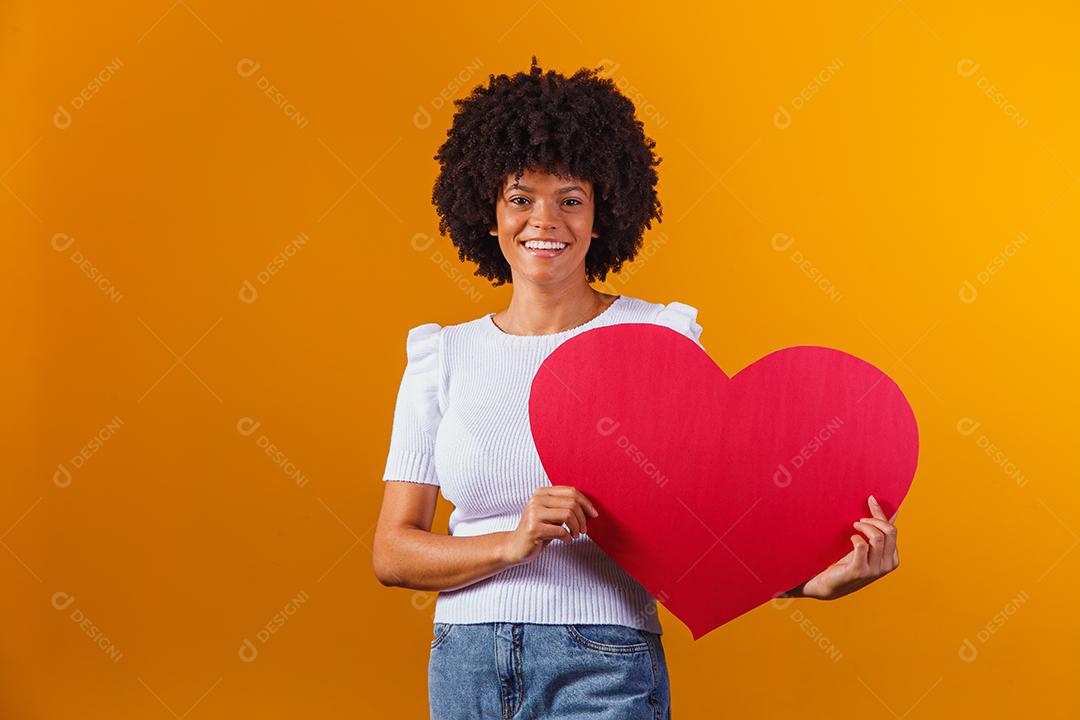 Mulher Afro sorridente segurando um grande cartão de coração vermelho