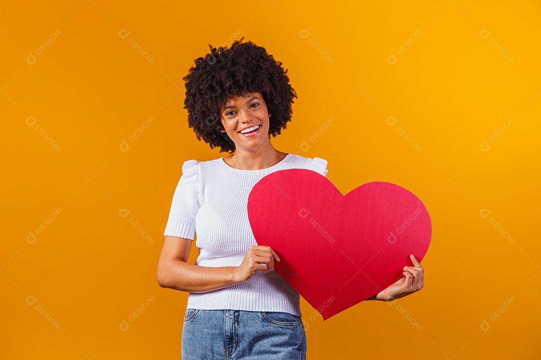 Mulher Afro sorridente segurando um grande cartão de coração vermelho