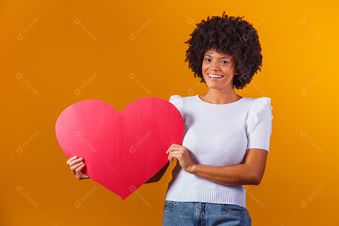 Mulher Afro sorridente segurando um grande cartão de coração vermelho