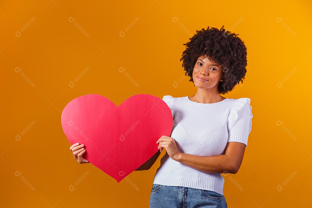 Mulher Afro sorridente segurando um grande cartão de coração vermelho