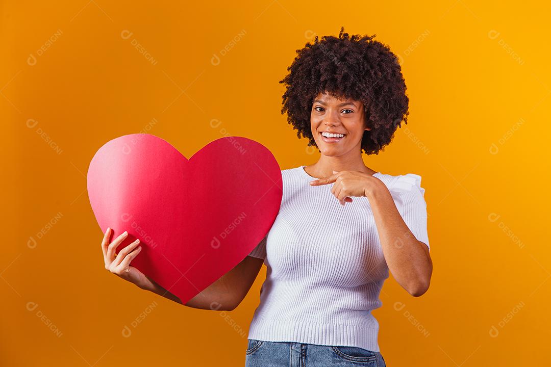 Mulher Afro sorridente segurando um grande cartão de coração vermelho